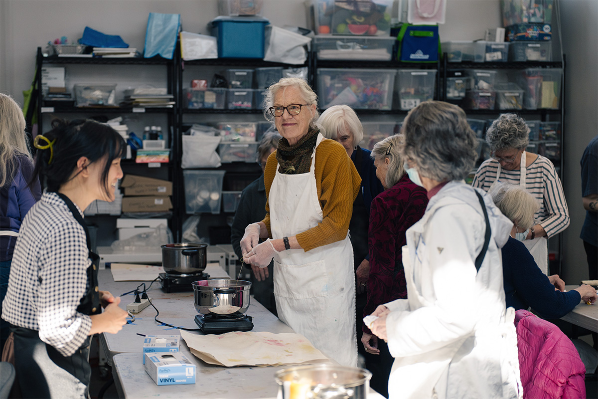 A group of people standing around a long table working on an art project using fabric and bowls of ink.