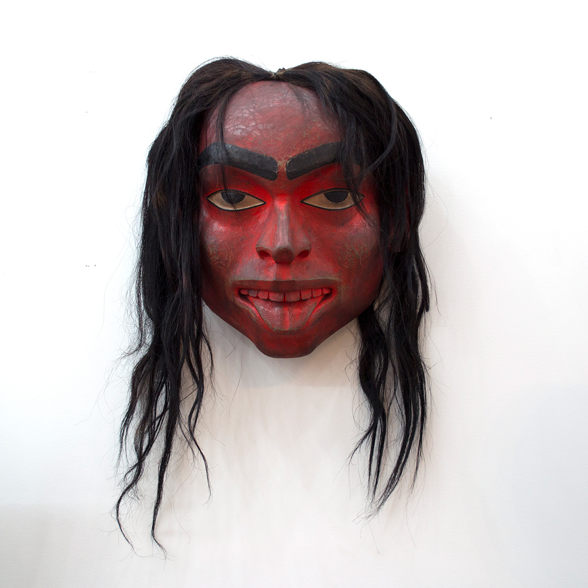 A dark red painted wooden human mask with long black hair
