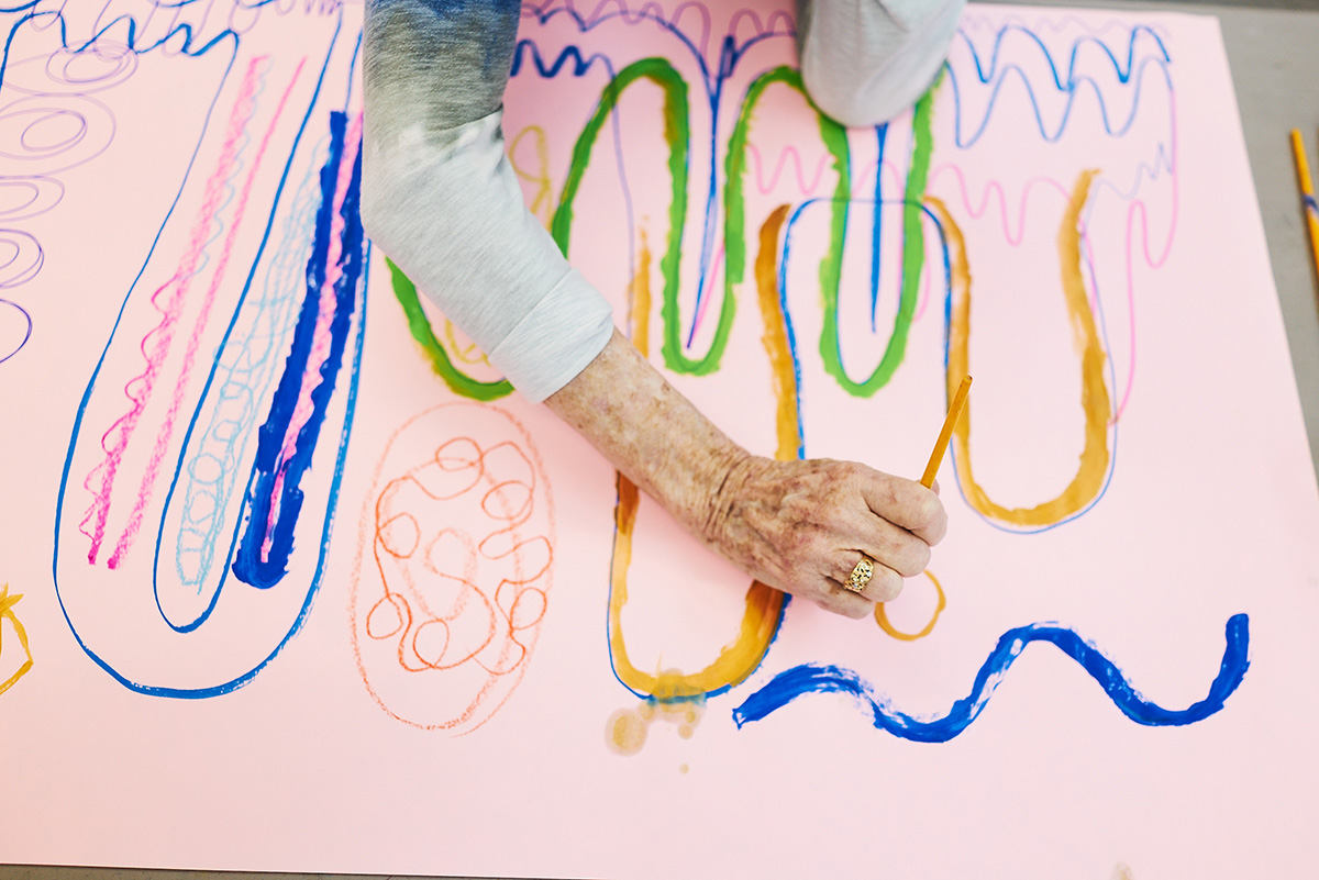 A person across a table reaches out and draws on a large sheet of paper