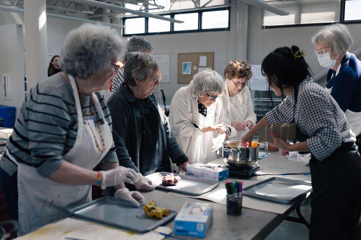 Older adults stnding working on an art project along a long table