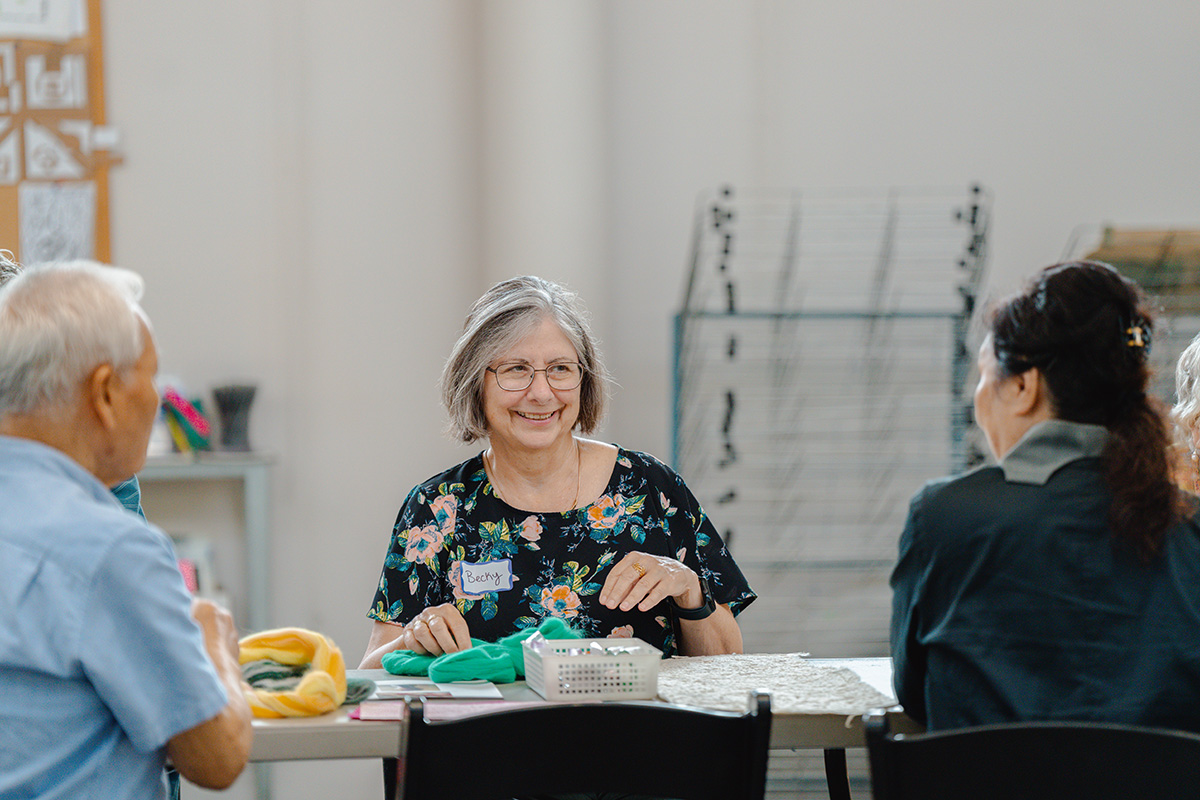 Older adults sitting at a table and working on an art project with fabrics in a well lit space 