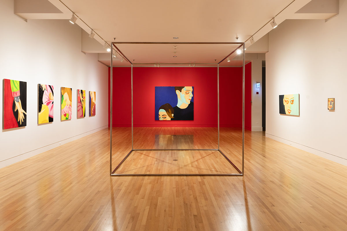 A gallery space with large, colorful paintings on the walls and a large metal frame cube in the center