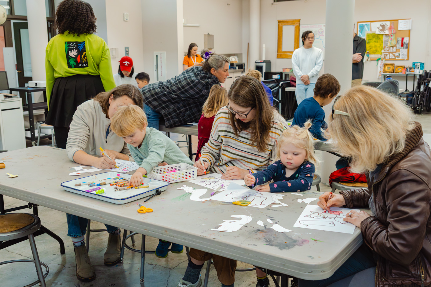 A group of children and adults work on an art project in a well-lit studio space
