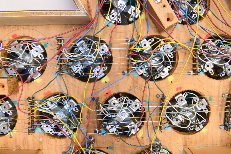 A view of a number of electrical circuits in cicular pockets on a piece of wood connected by wire