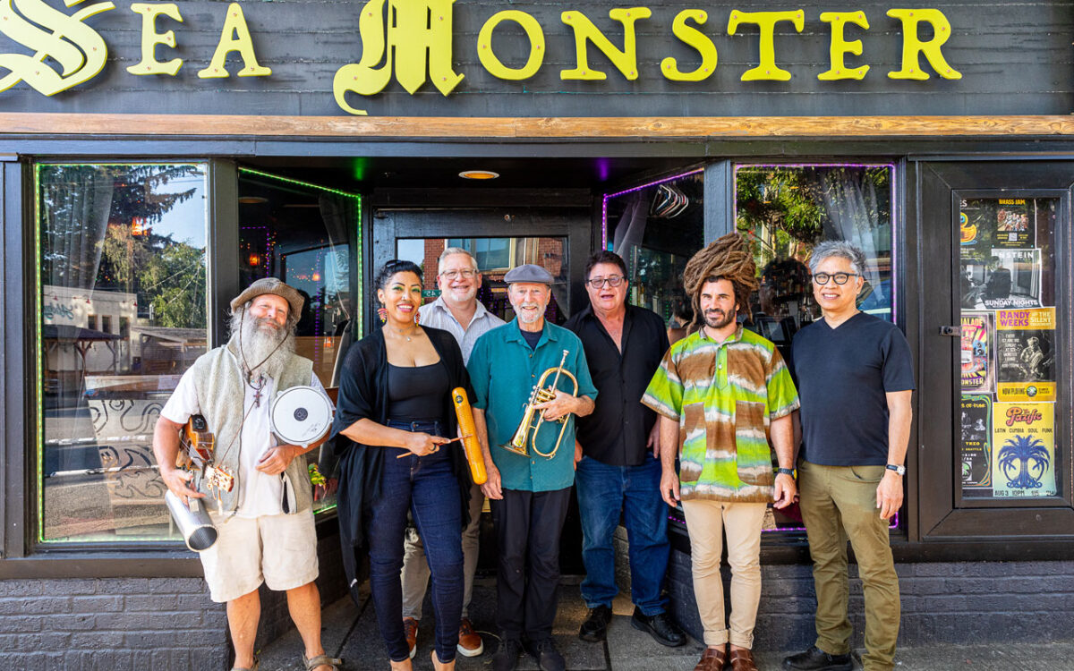 A diverse group of musicians posing outside a venue with a sign reading 'Sea Monster'