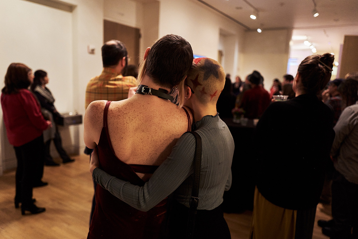 The backs of two people standing together with one's arm around the other as part of a larger group