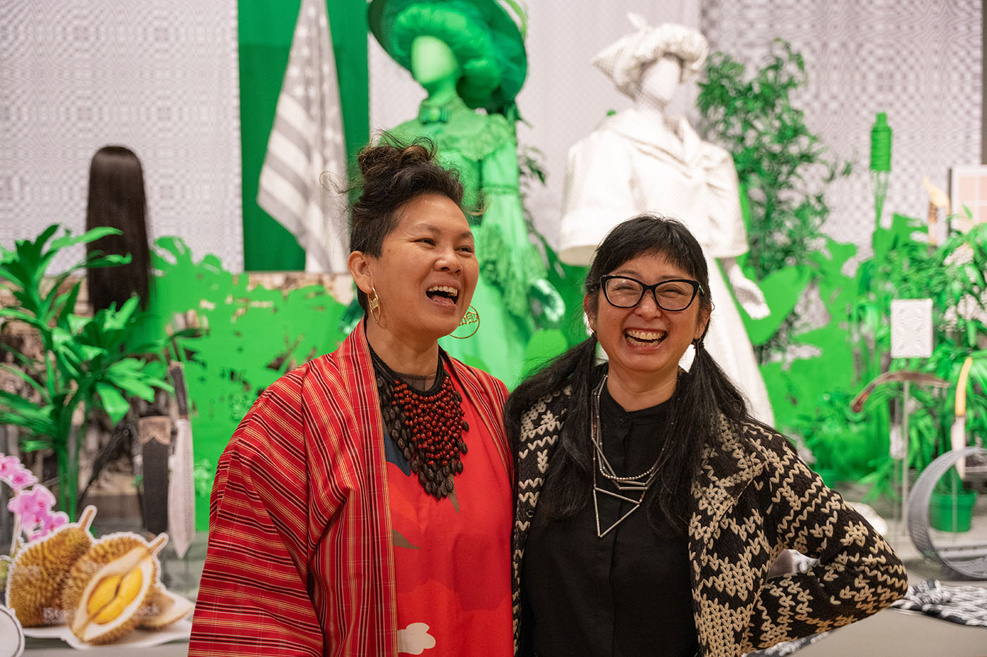 Two Asian women standing together and smiling in front of a large art installation