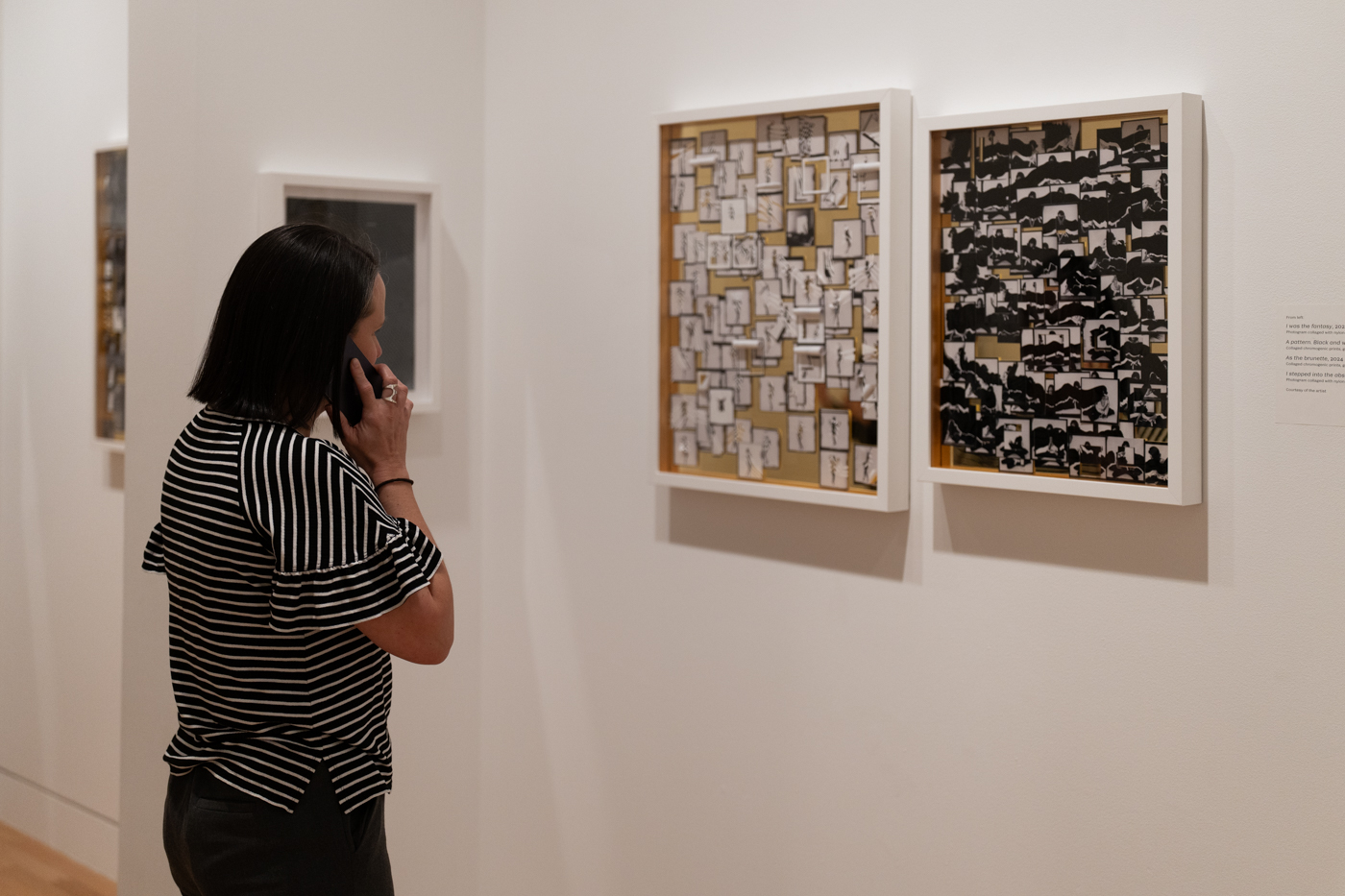 A person holding a phone up to their ear while they look at two collage based pieces of art hanging on a wall in front of them