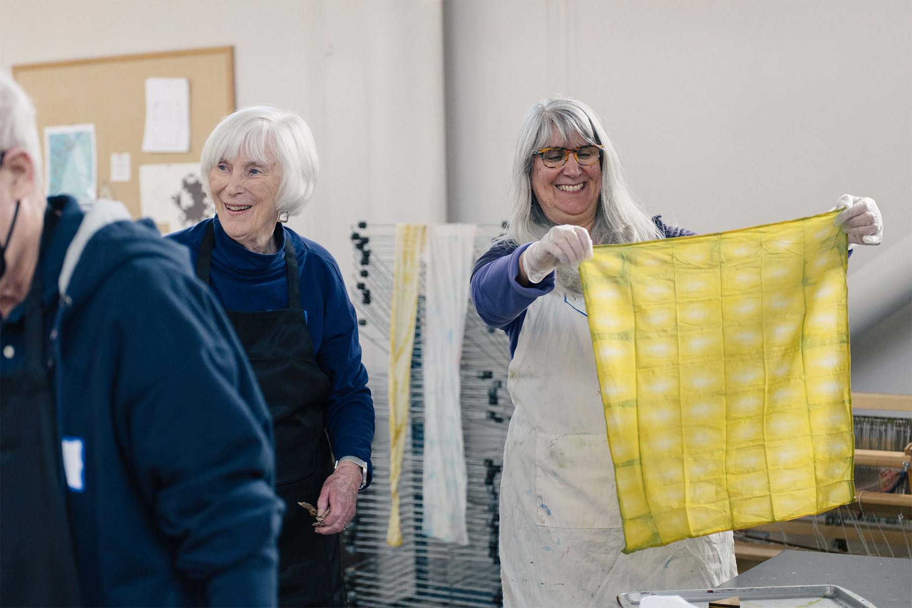 People chatting and smiling while looking at a freshly dyed yellow handkerchief