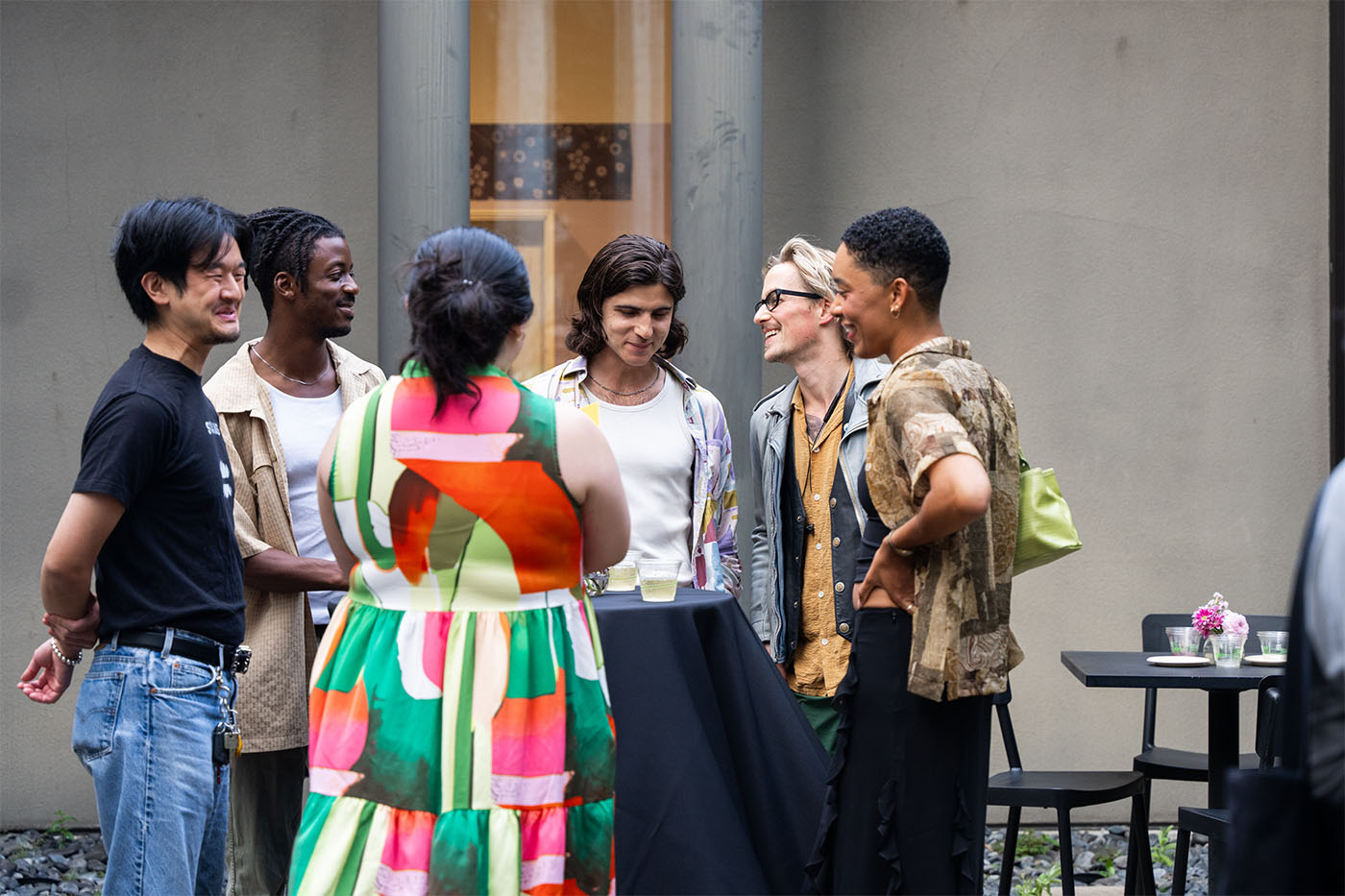 Younger people standing and chatting around a table in an outdoor courtyard area
