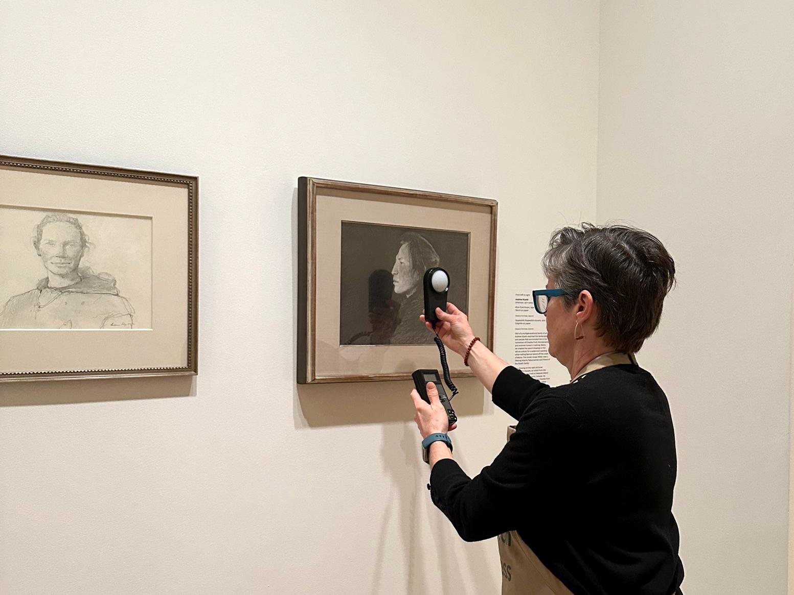 A person holds a small light reader device up to a work of art on a wall
