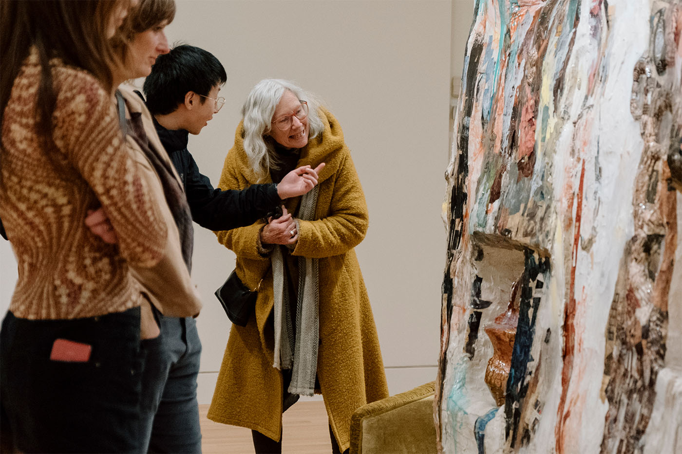 A group of standing people chatting and looking at a large sculptural artwork on the right side of the frame
