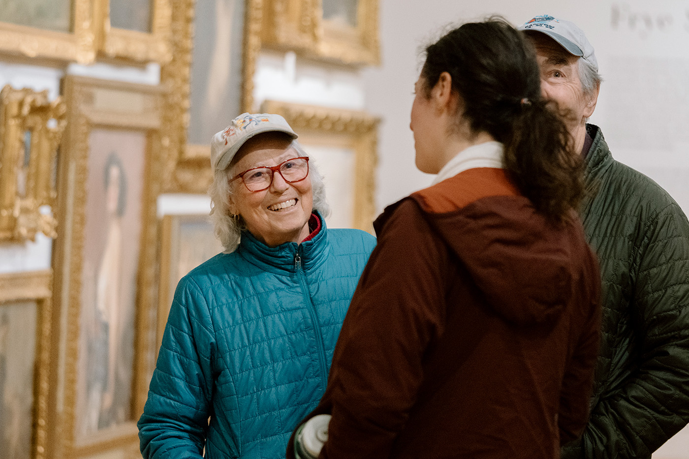 People chatting in a large room in front of paintings in opulent frames