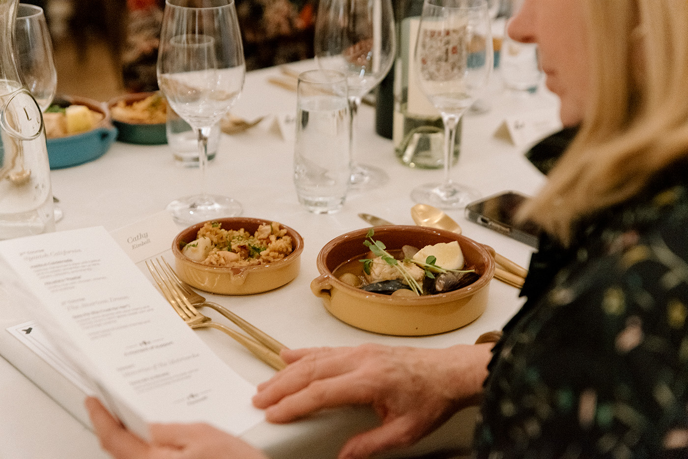 A plate of food in front of a person on a well laid white tablecloth