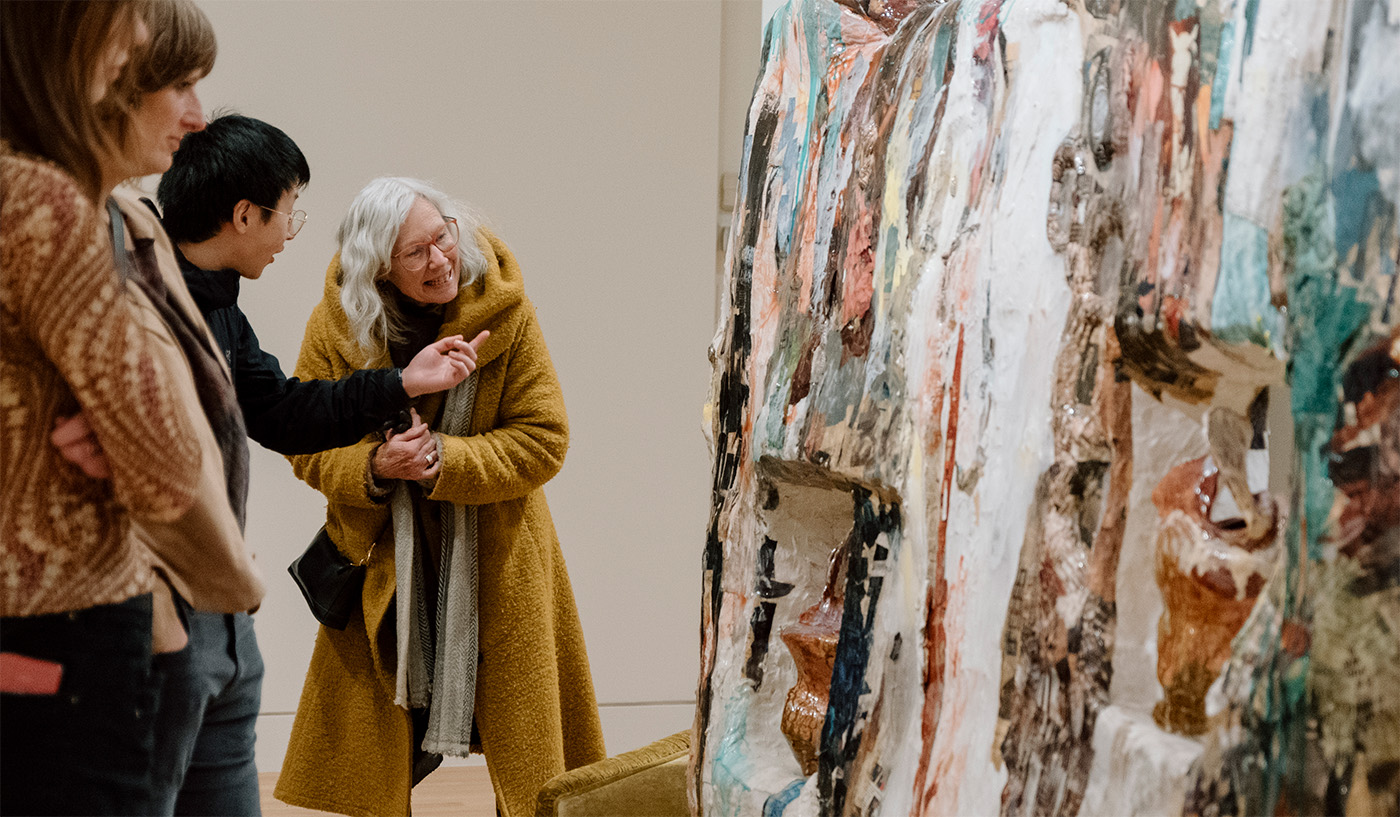 A younger man and older woman chat while looking at a large sculptural artwork in a museum space