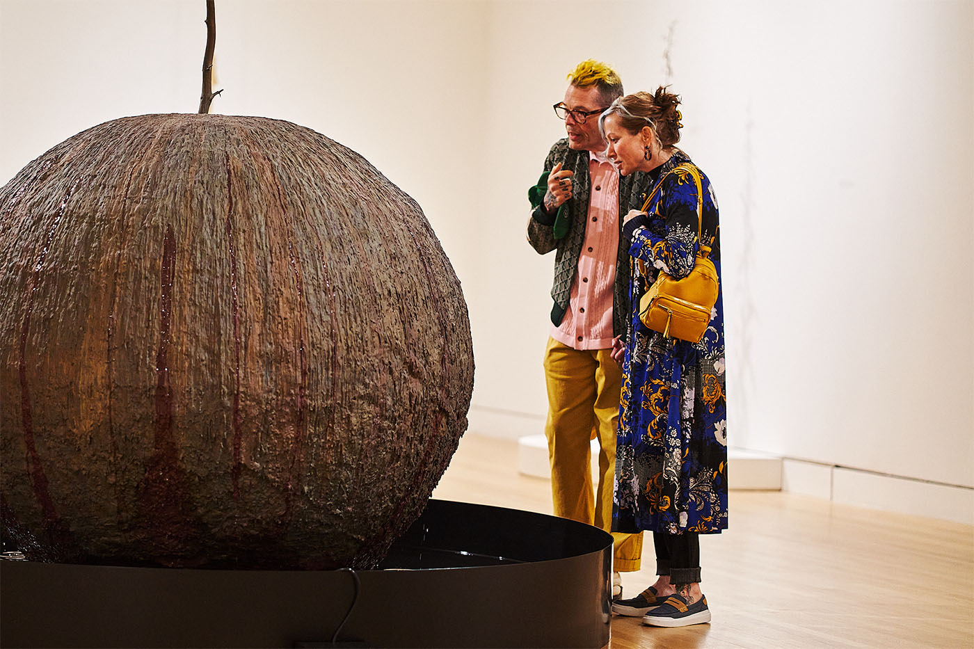 Two people in colorful party clothing looking at a large, spherical artwork