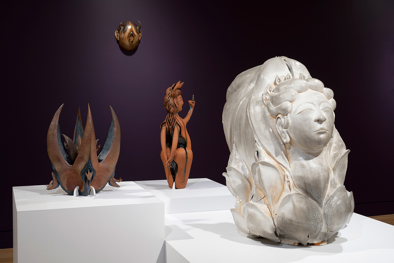 Ceramic sculptures on pedestals in a gallery in front of a purple wall