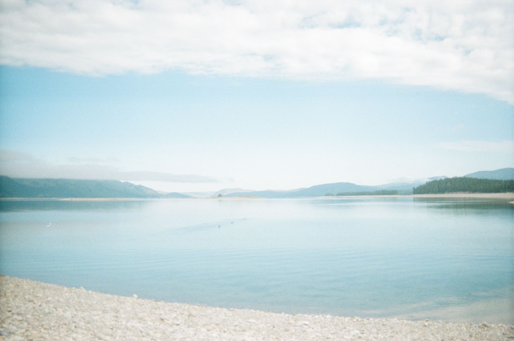 Lake with sandy beach in the foreground and mountains in the background