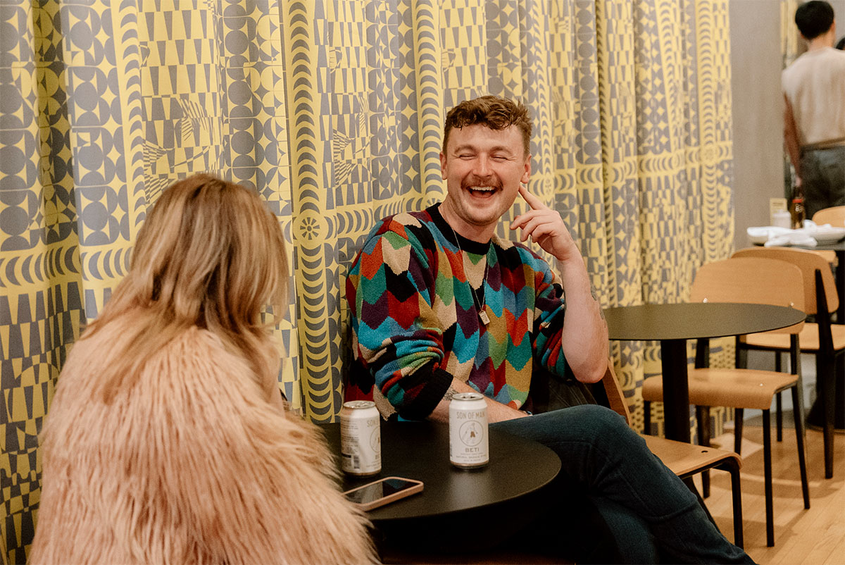 People smiling and chatting at a cafe table in front of a yellow curtain