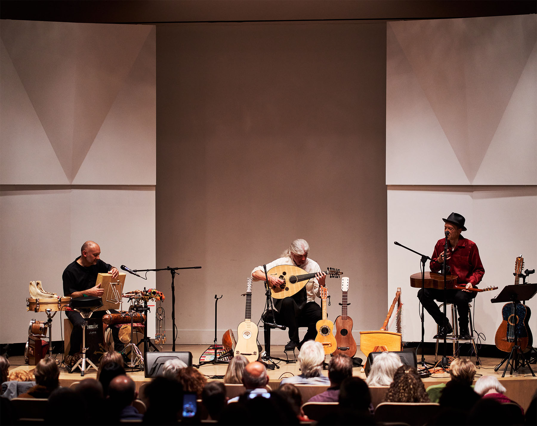 Three people surrounded by and playing traditional looking and stringed instruments on a stage