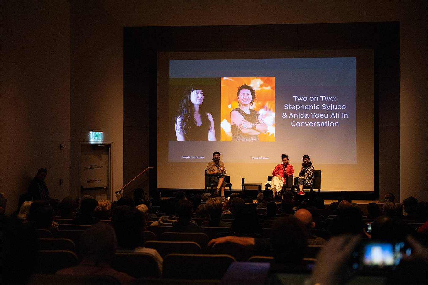 View from the back of an auditorium of three people seated on stage 
