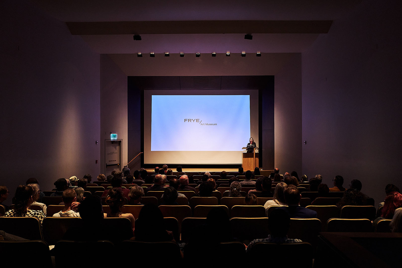 The Frye auditorium with a person at a podium on stage and people sitting in seats
