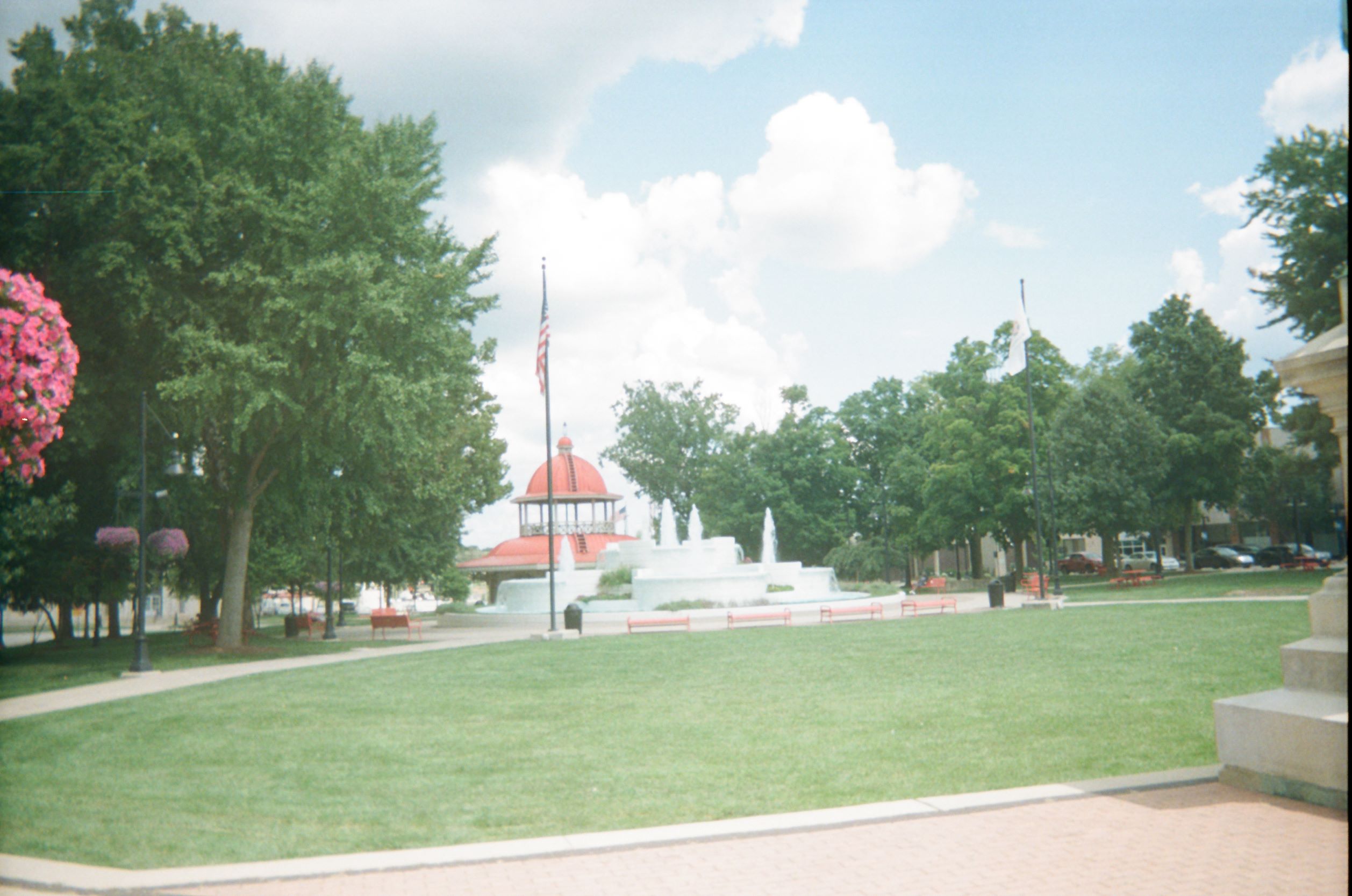 Pavilion with red roof and white structure, surrounded by leafy trees and an open grassy area