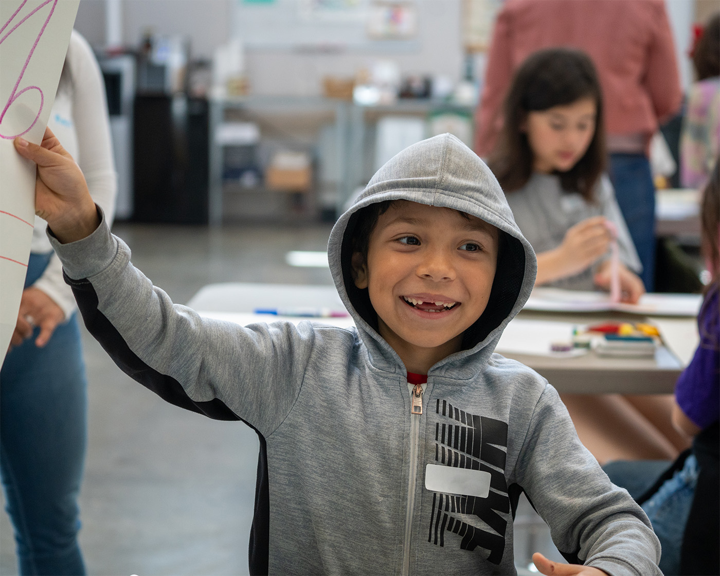 A child smiling and holding up a piece of their artwork extending out of the frame