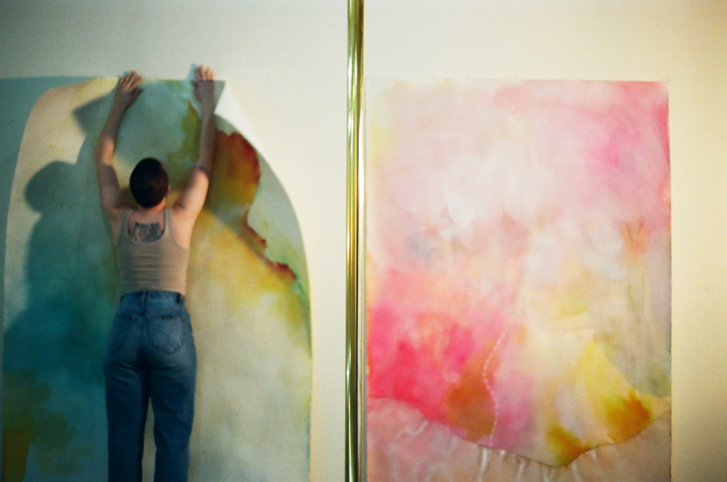 Photo of Lydia Jewel Gerard hanging a bright colorful artwork on a wall next to another piece
