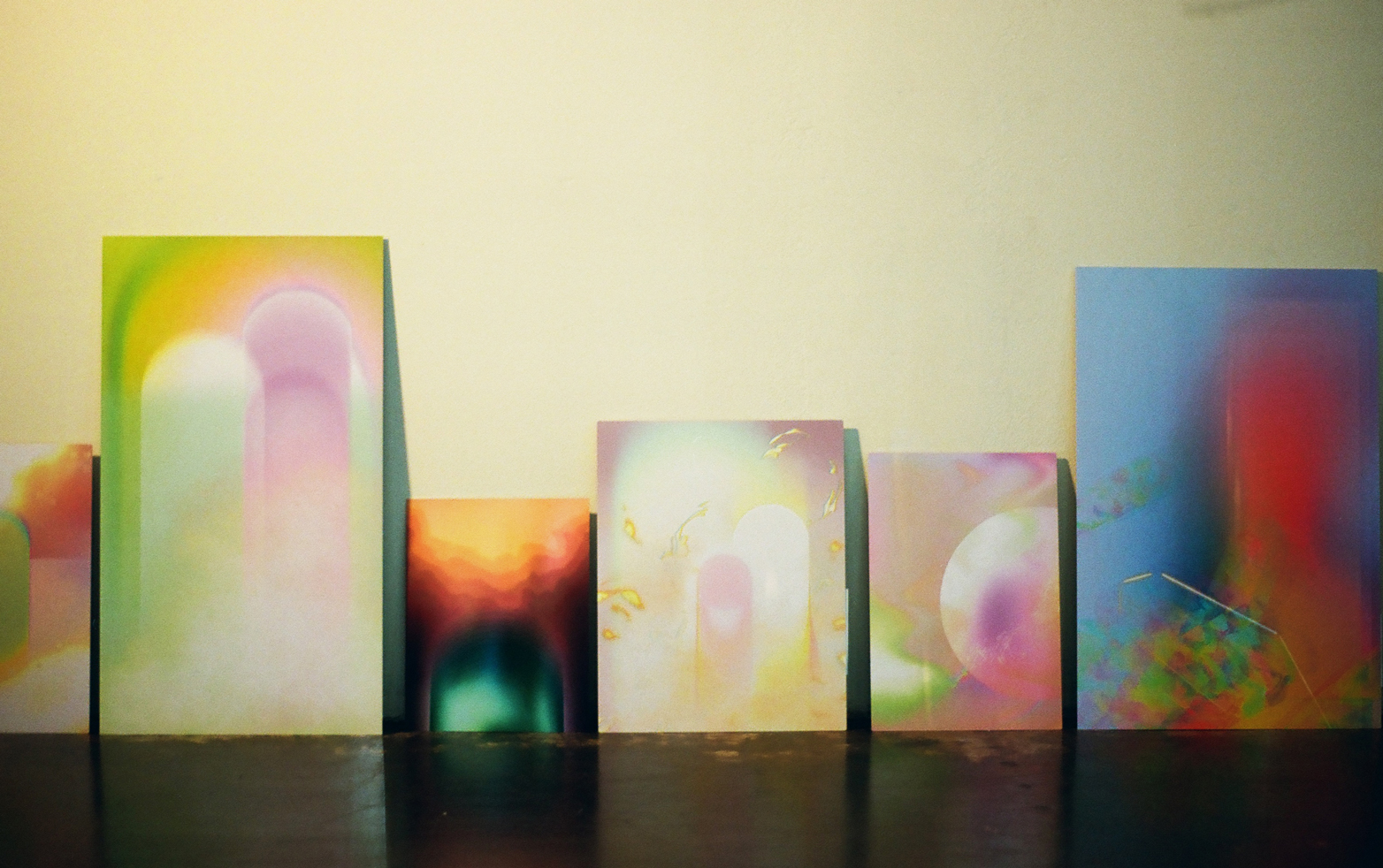 Photo of six bright colorful artworks by Lydia Jewel Gerard lined up against a wall