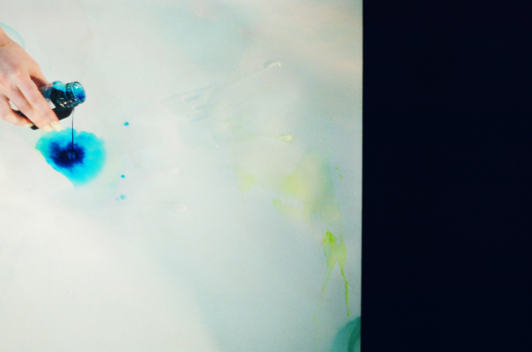 Photo Lydia Jewel Gerard's hand dripping blue pigment from a bottle onto a large piece of paper