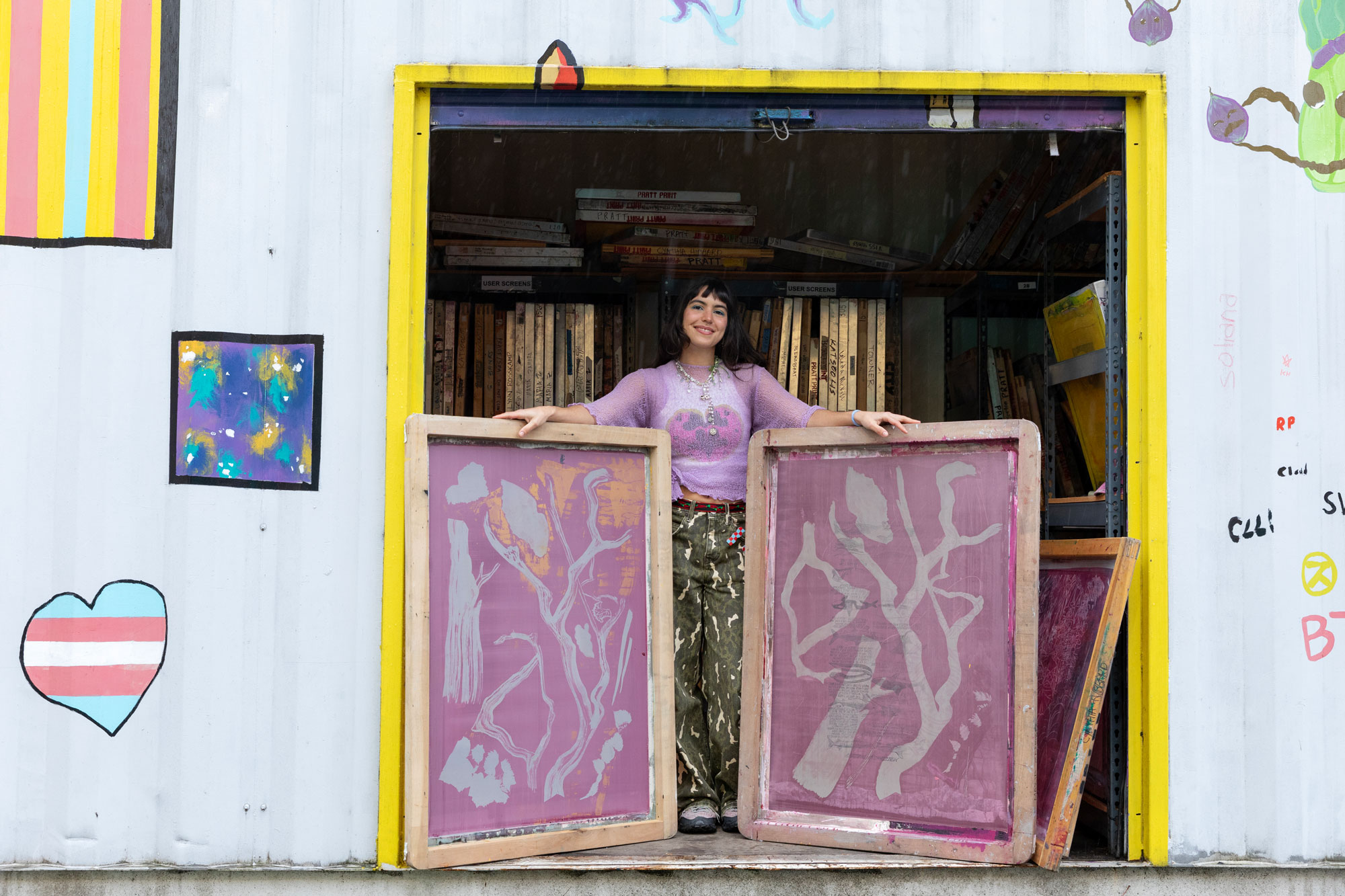Artist María Zamora standing with two large screens for screenprinting which come up to just above her waist