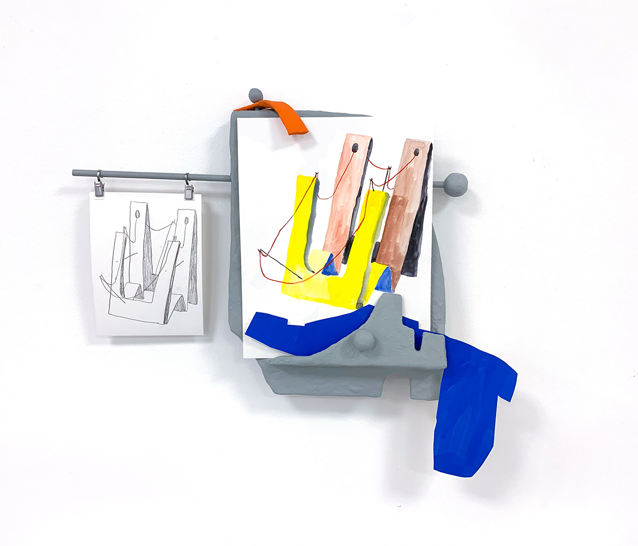 An artwork mounted on a white wall made of bits of household material painted gray holding pieces of paper colored with a geometric design