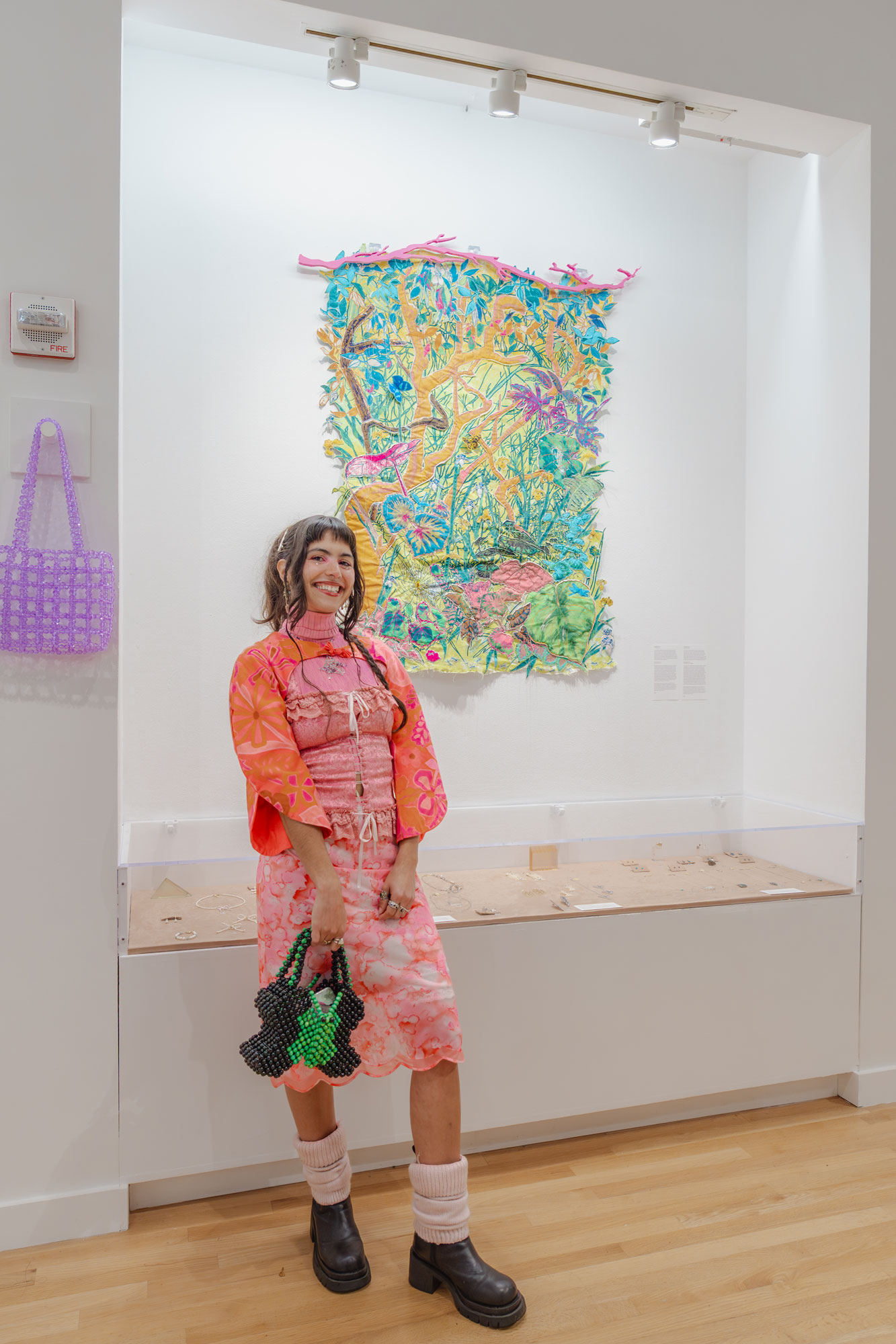 Artist María Zamora standing by her brightly colored tapestry "Los Cínaros" hung in the alcove of the Frye Museum Store