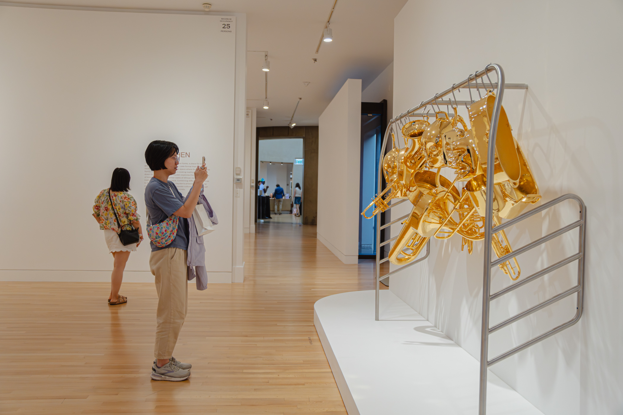 A person taking a phone photo of a gold and steel sculptural artwork