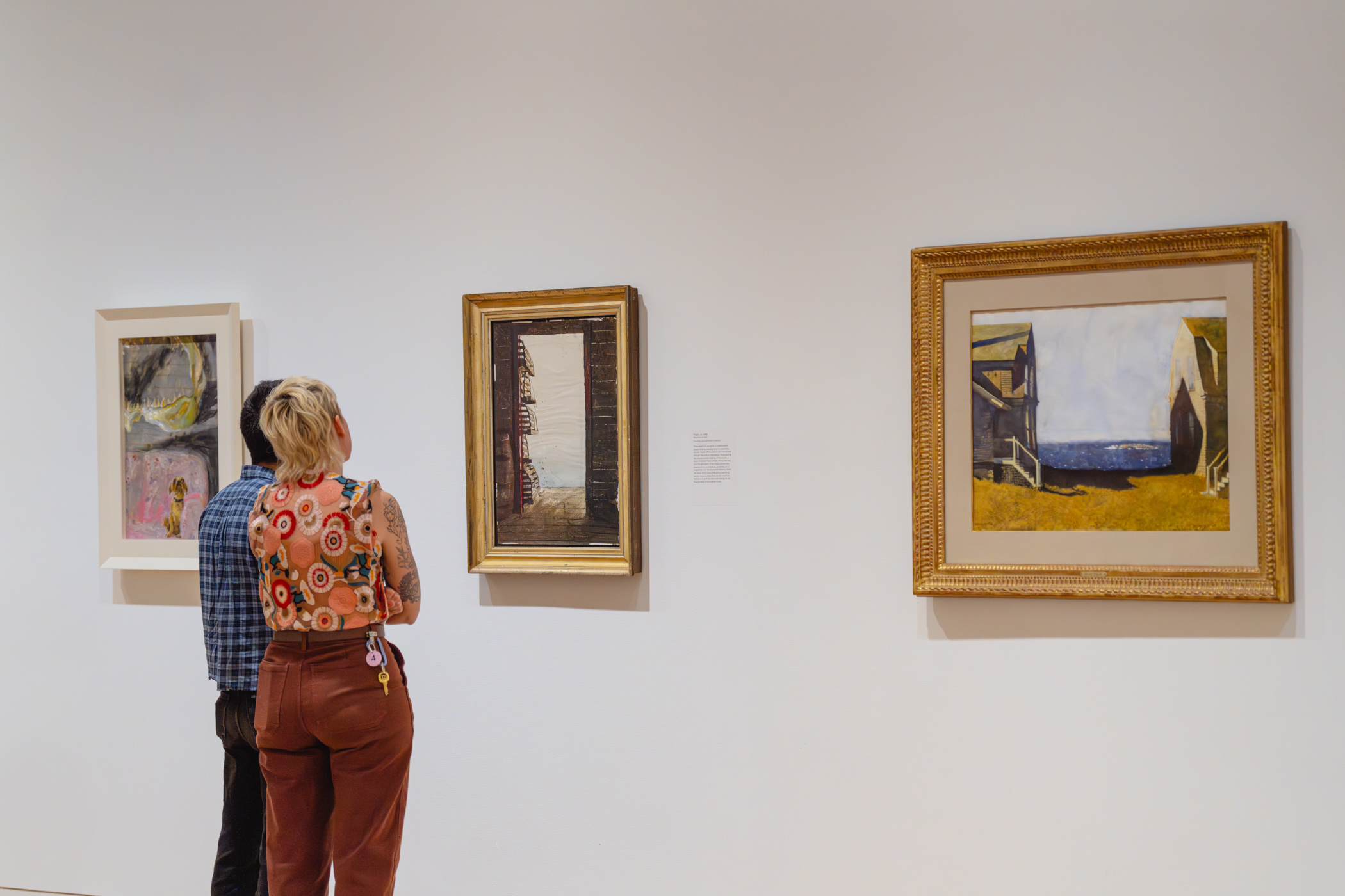 People looking at oil paintings mounted on a wall