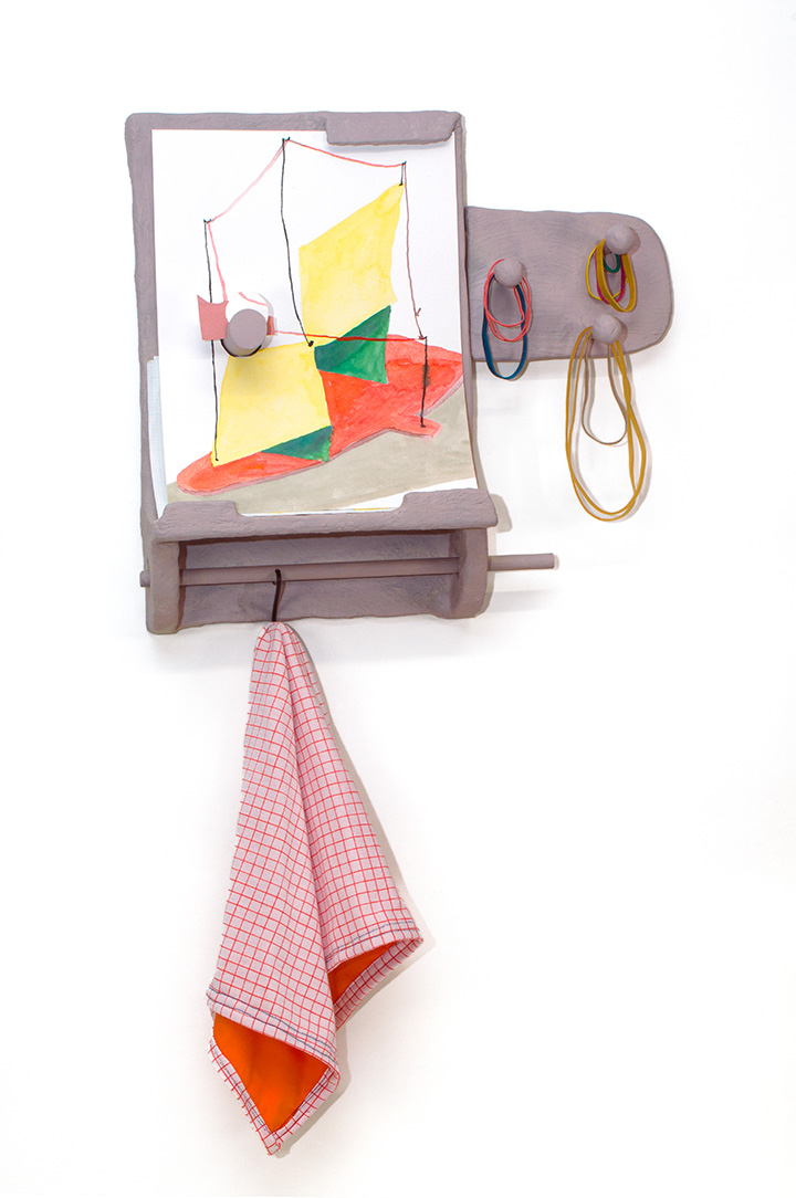 An artwork mounted on a white wall made of bits of household material painted with a reddish tint. Colored paper, rubber bands, and a cloth are hanging off in various positions