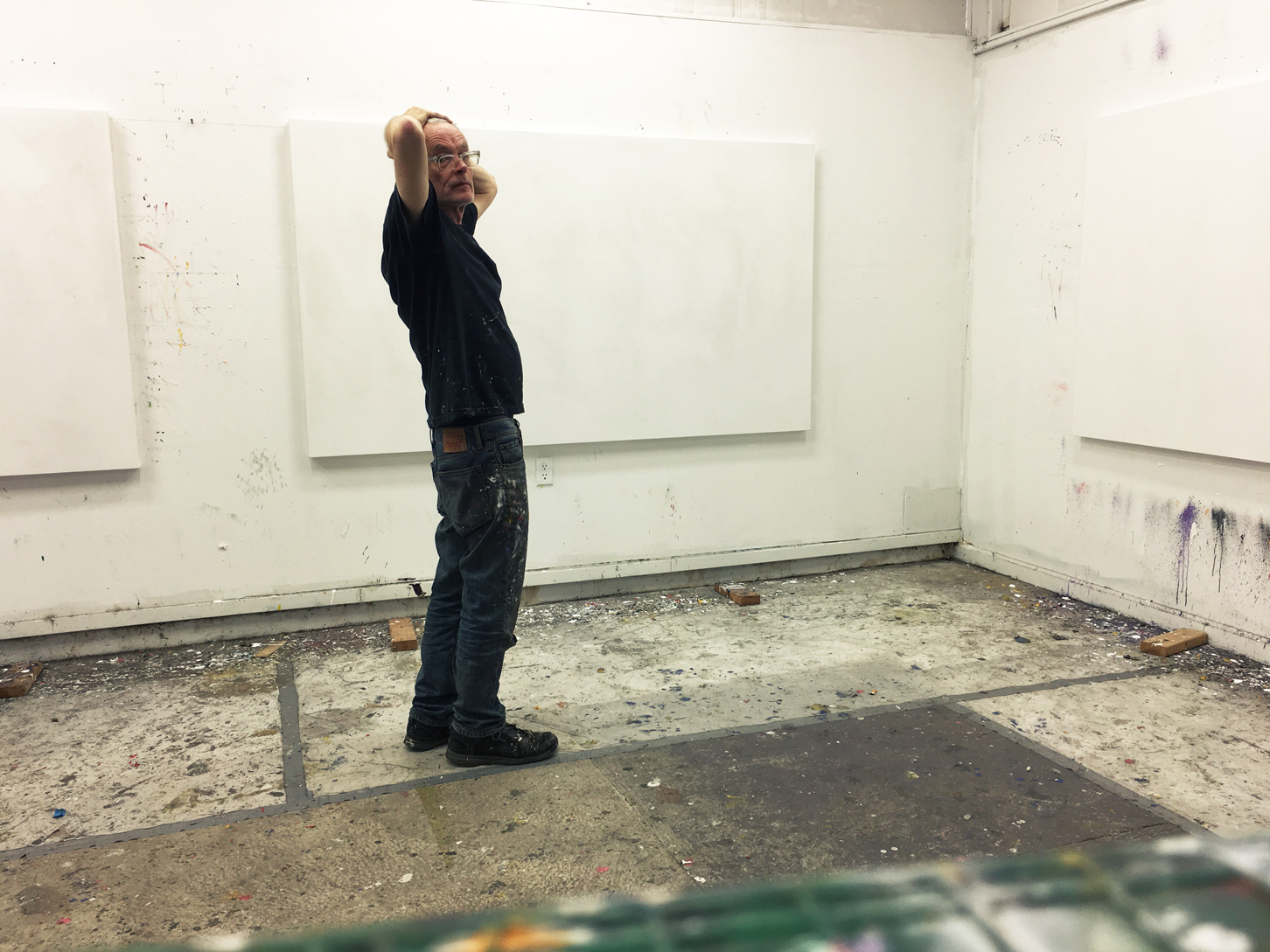 Photo of Ken Kelly in his studio looking at three white canvases on the walls