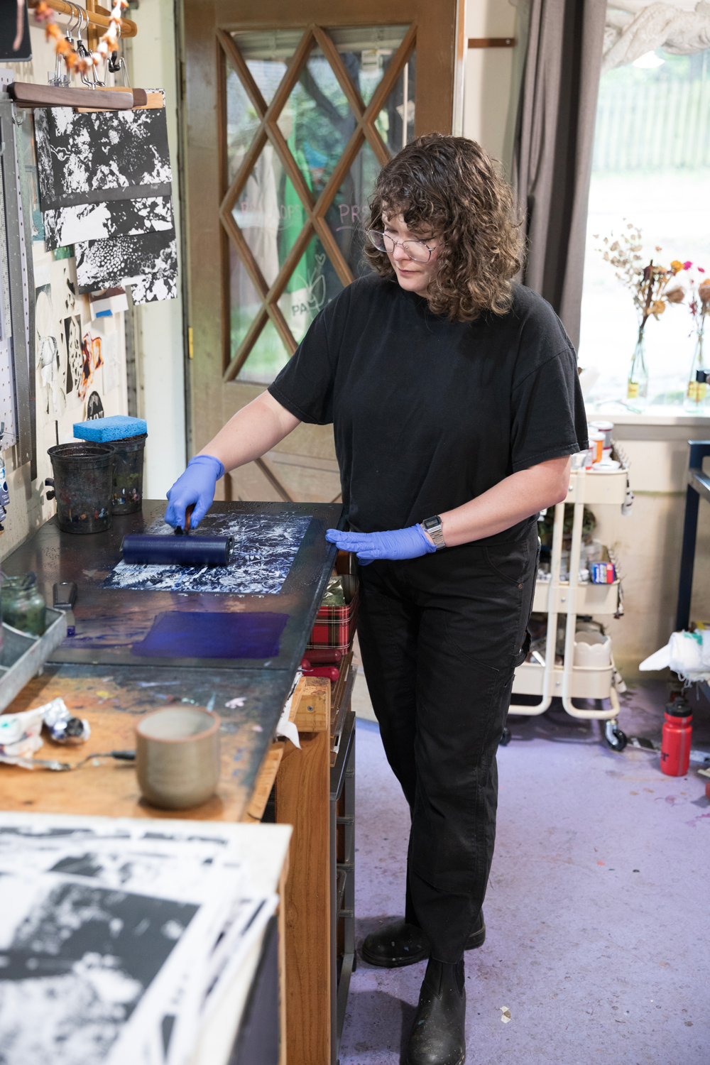 Photo of Shannon Bodrogi in their studio in the process of making a paper lithograph, rolling ink with a roller