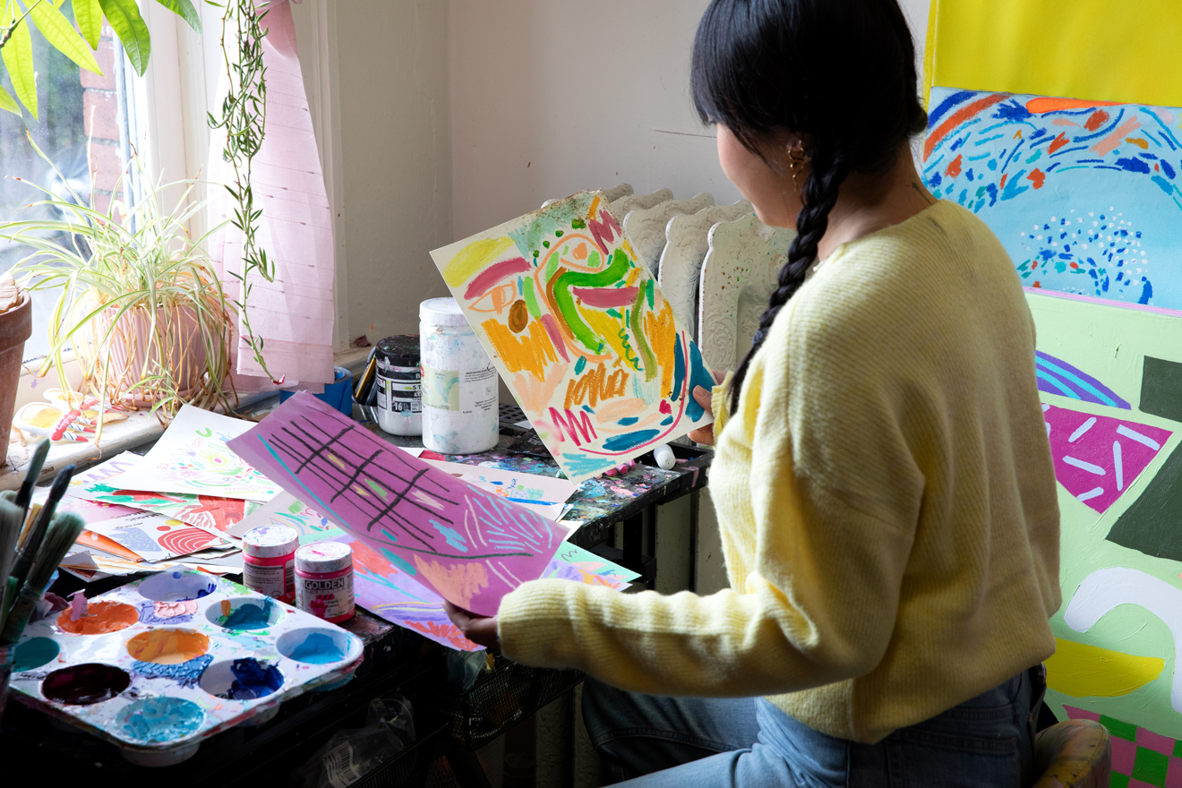 Photo of Nikita Ares, a woman with dark brown hair, sifting through her art on a table