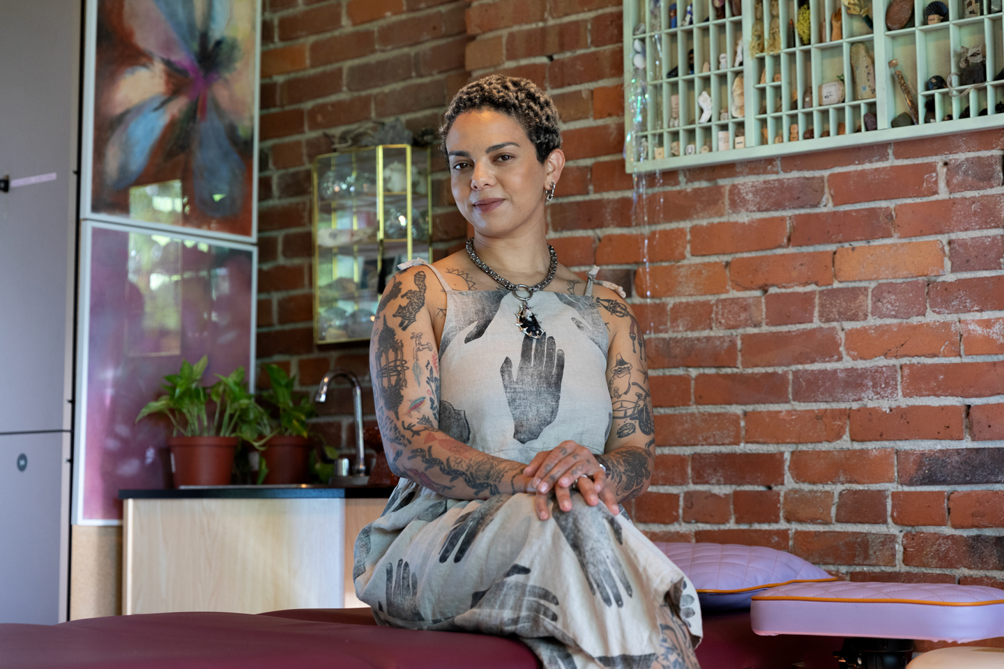 Emma Kates-Shaw sitting on a tattoo table at their studio looking directly at the camera