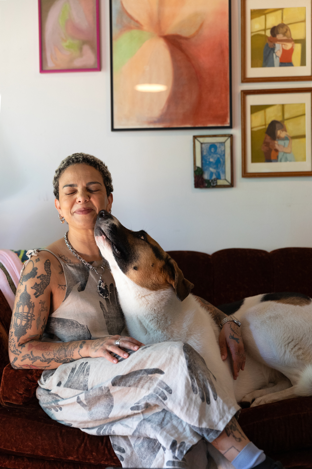 Emma Kates-Shaw sitting on a couch with a dog cuddling with her and sniffing her face
