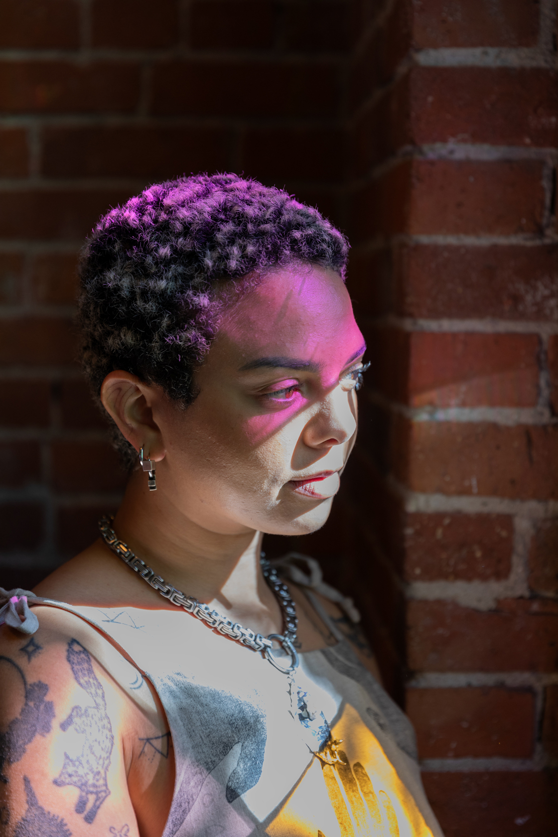 Photo of Emma Kates-Shaw with light illuminating their face and a purple cast lighting the top of their head