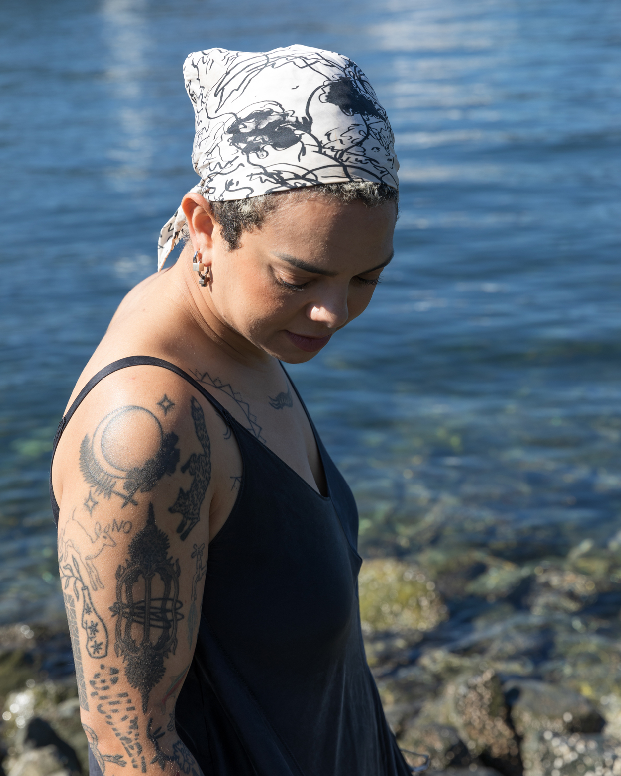 Emma Kates-Shaw looking down at the ground at a rocky beach with the water behind her