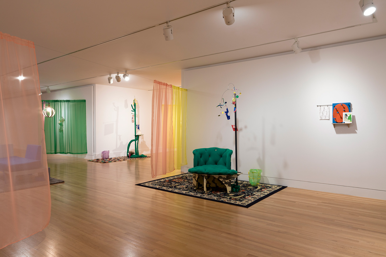 A larger, long room in an art gallery with a variety of abstract, sculptural artworks and hanging curtains