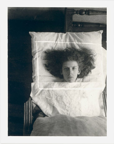 A black and white photo of a person on a bed with their hair splayed out around their head on a pillow