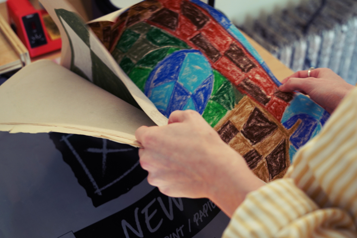 Photo of hands holding a portfolio of artwork showing a colorful piece with a checkerboard pattern
