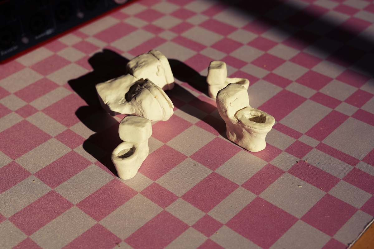 Photo of small white toilet figures sitting on a pink and gray checkerboard background