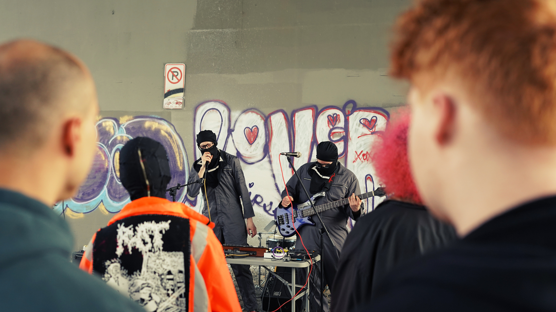 Photo of two people of the band Scum Wife performing outside seen beyond the audience of people watching