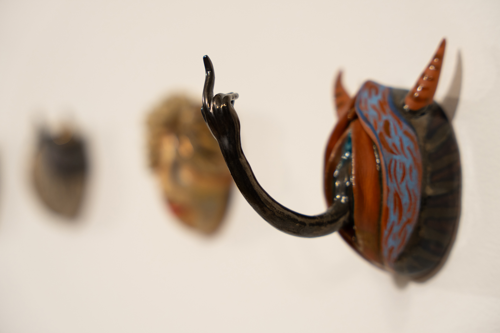 Small ceramic mask whose face is a vulva and has horns and an arm coming out giving the middle finger